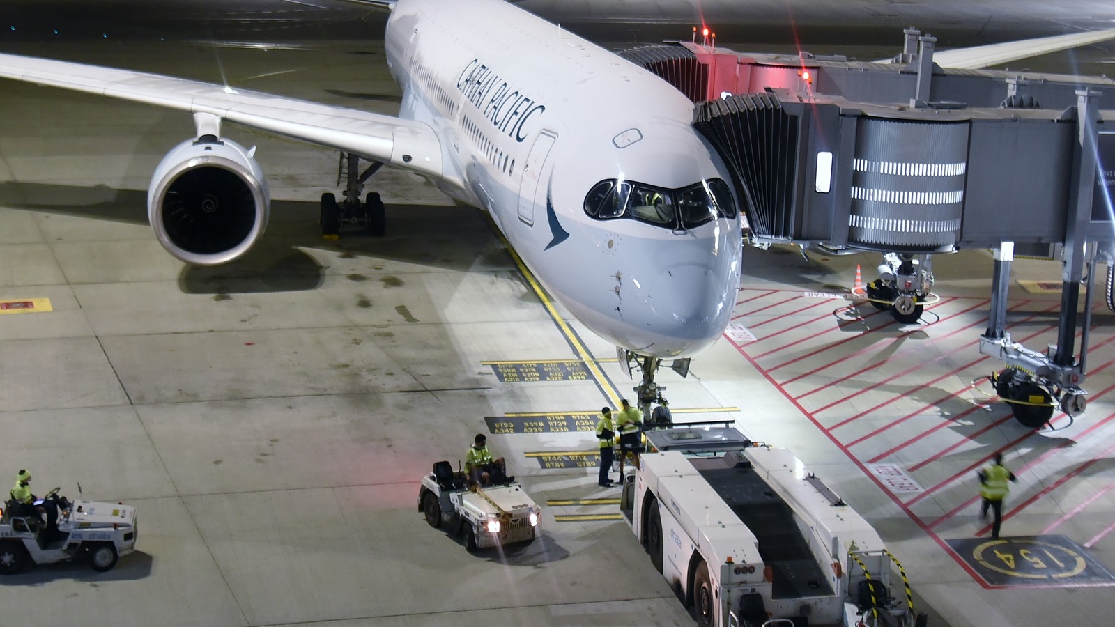 A Cathay Pacific Airbus A350 at a gate with a jet bridge attached and ground crew working beneath the nose