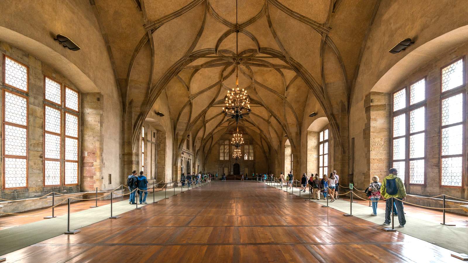 Vladislav Hall in Prague Castle with its ribbed vaulted ceiling, chandeliers and visitors along roped walkways