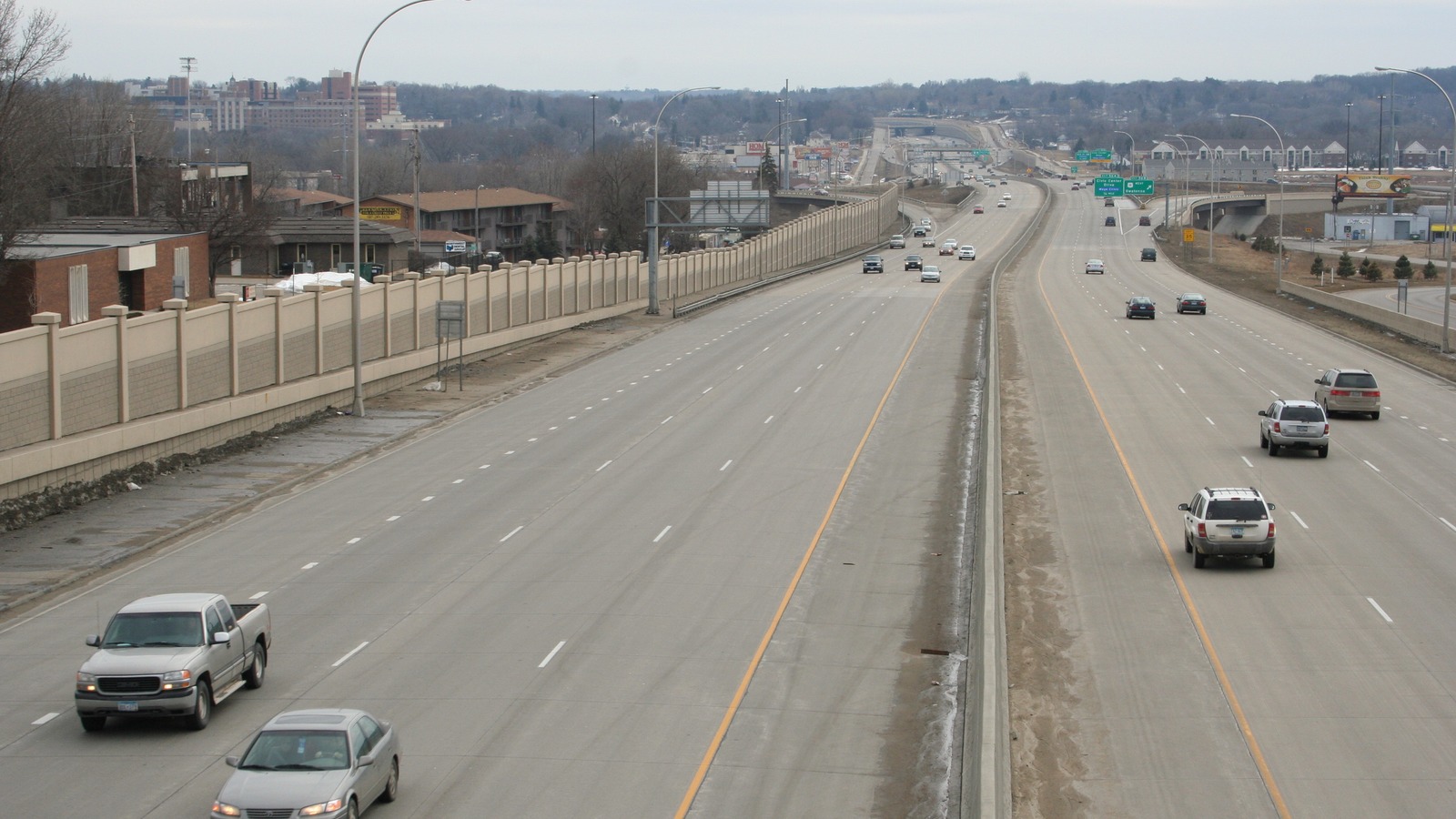 Looking south along the divided carriageways of US Highway 52 in Rochester, Minnesota, with a noise wall on one side, green overhead exit signs ahead and light traffic on both sides