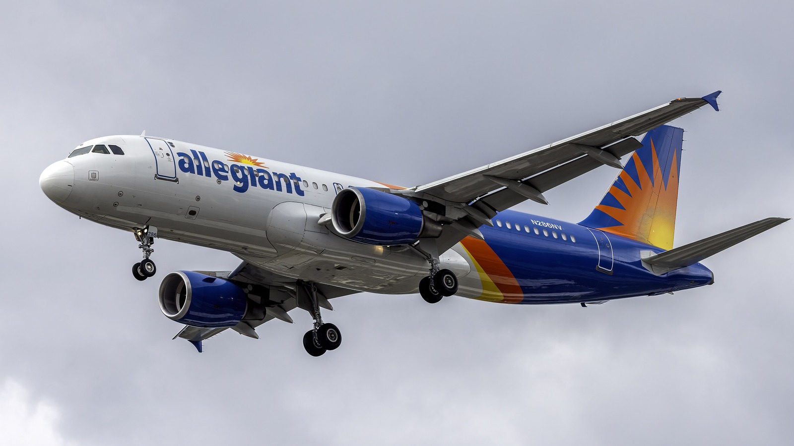 An Allegiant Air Airbus A320 on final approach with landing gear down, the allegiant titles and sunburst tail clearly visible against a grey sky.