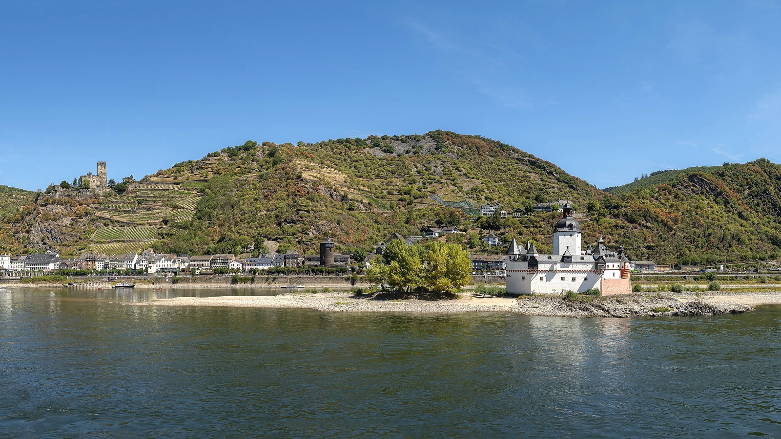 Pfalzgrafenstein castle standing on an exposed gravel bar in the Rhine at Kaub during 2026 low water, with vineyards and Kaub town behind.