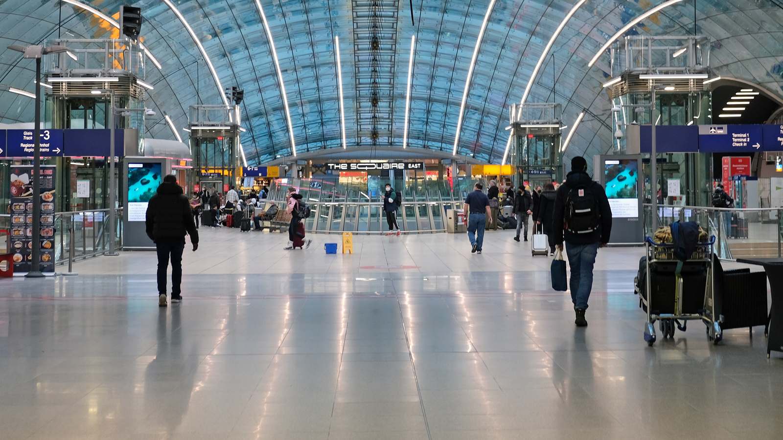 Glass vaulted hall of Frankfurt Airport long distance train station with a sign pointing to Terminal 1 check-in and travelers with luggage.