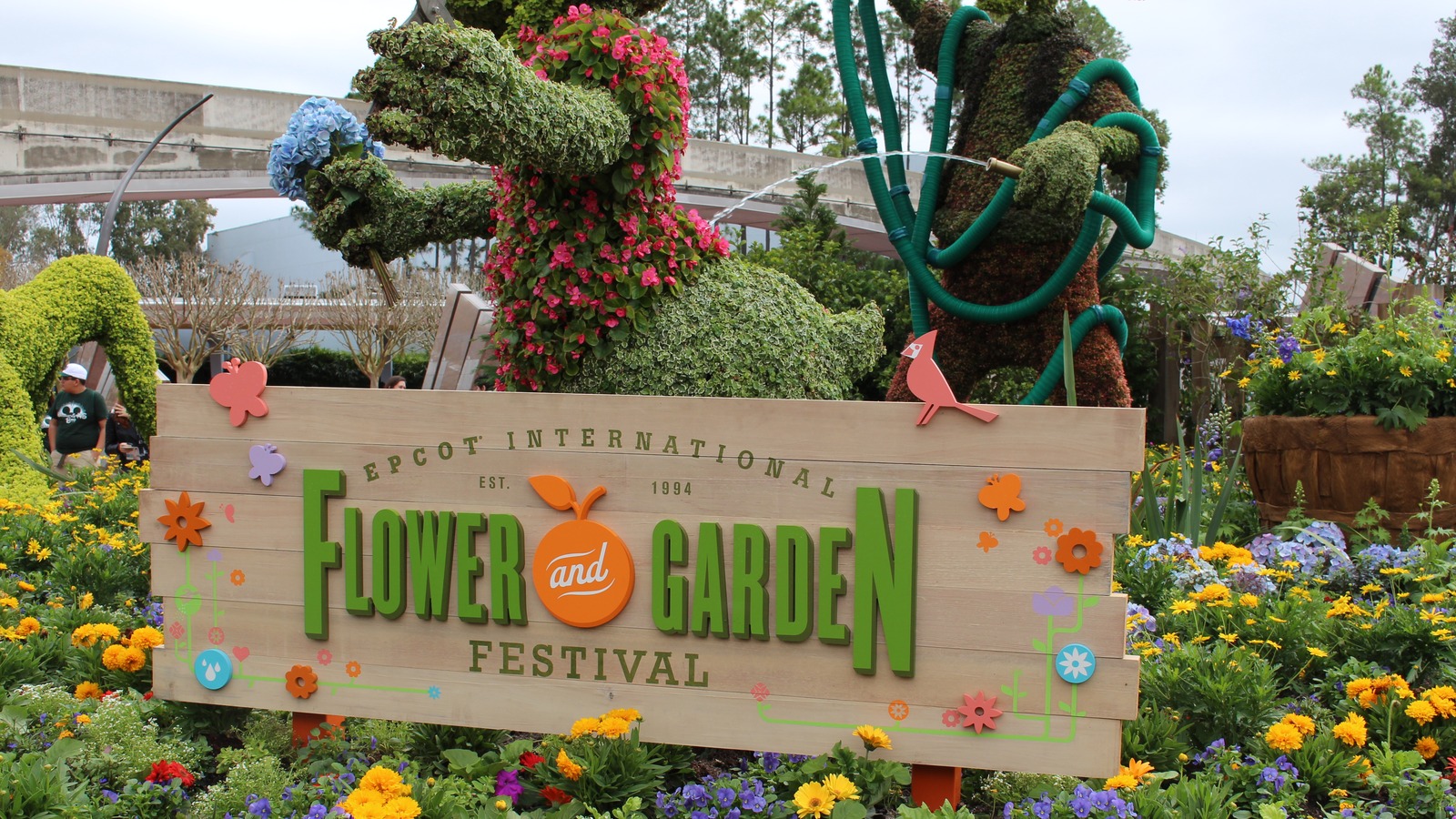 Goofy topiary watering flower beds behind the wooden EPCOT International Flower and Garden Festival entrance sign