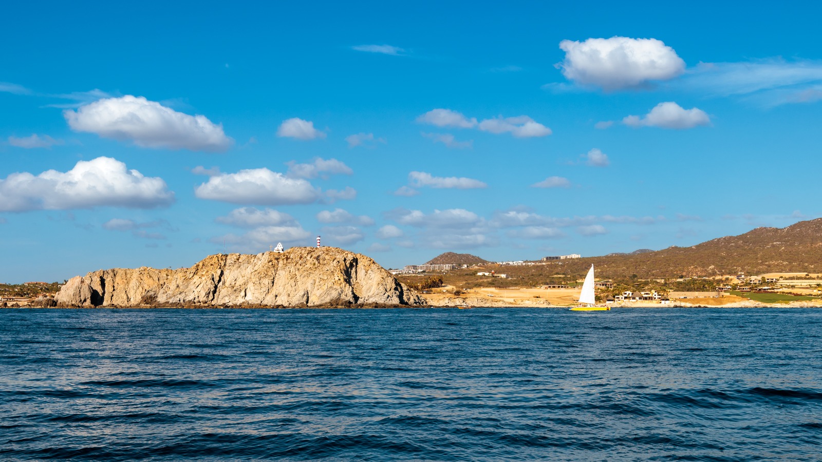 Rocky coastline with a small church and a striped lighthouse east of Cabo San Lucas near the southern tip of Baja California under a blue sky