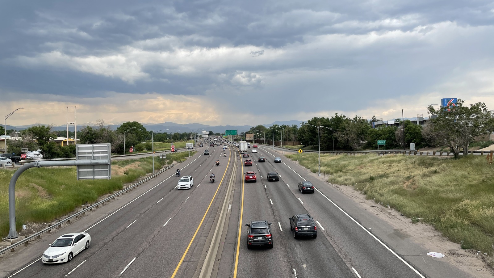 Westbound Interstate 70 in west Denver seen from an overpass, six lanes of light traffic running toward the Front Range foothills under a heavy grey sky