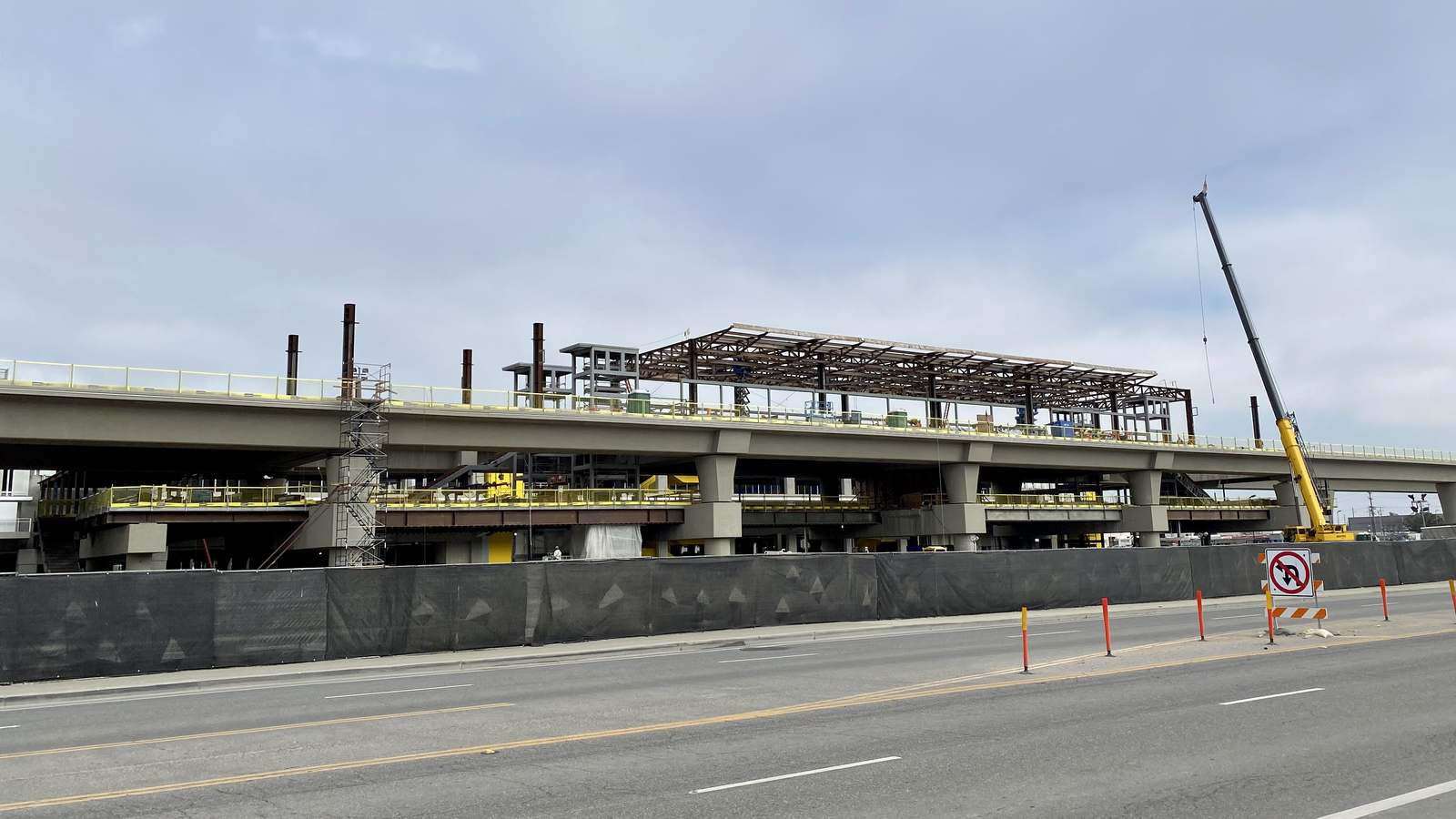 Elevated concrete guideway and station structure of the LAX automated people mover under construction beside a road, with a crane at right.