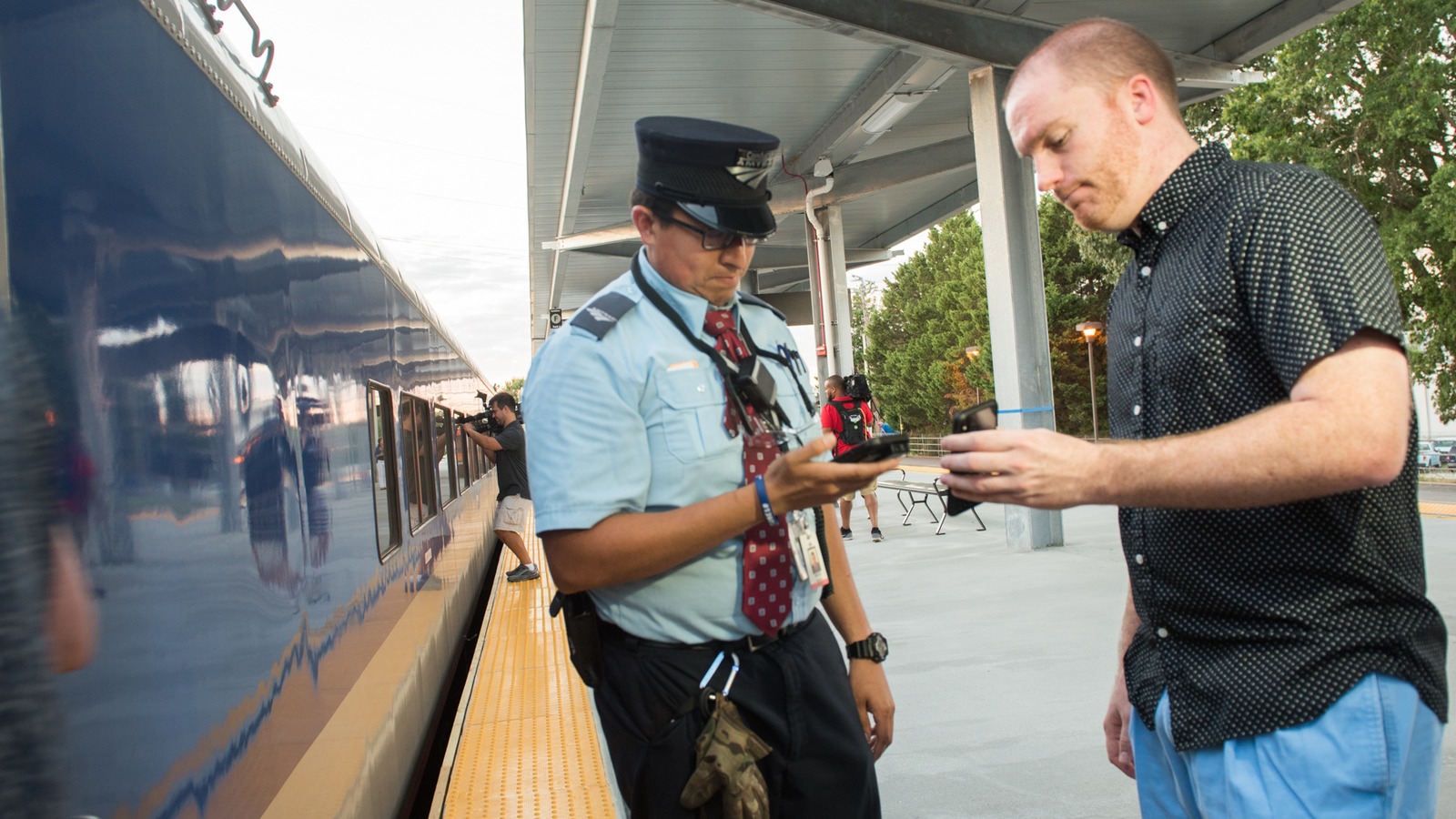 NC By Train conductor scans a passenger phone beside a train at Raleigh Union Station
