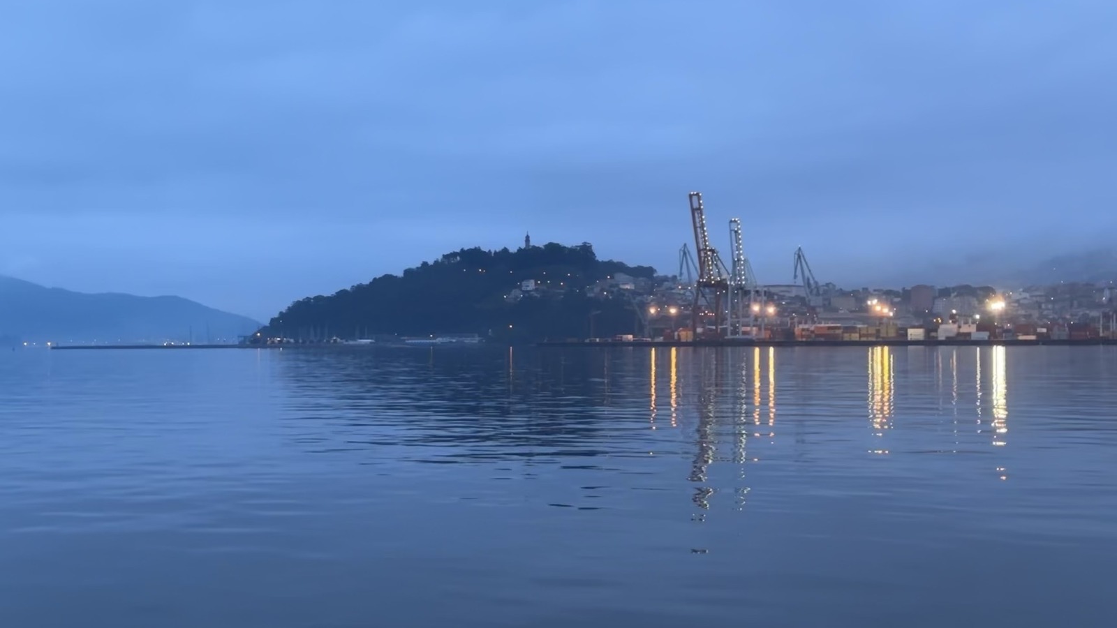 Port of Vigo harbor cranes and lights reflected on calm estuary water at dusk