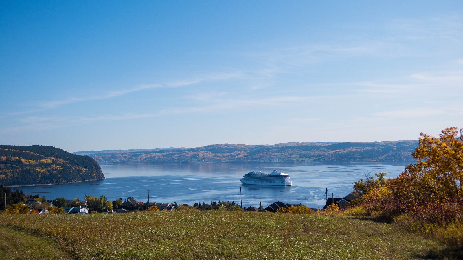 A cruise ship on the Saguenay fjord off La Baie in autumn, with the hills of the fjord in fall colour and the houses of the town along the near shore