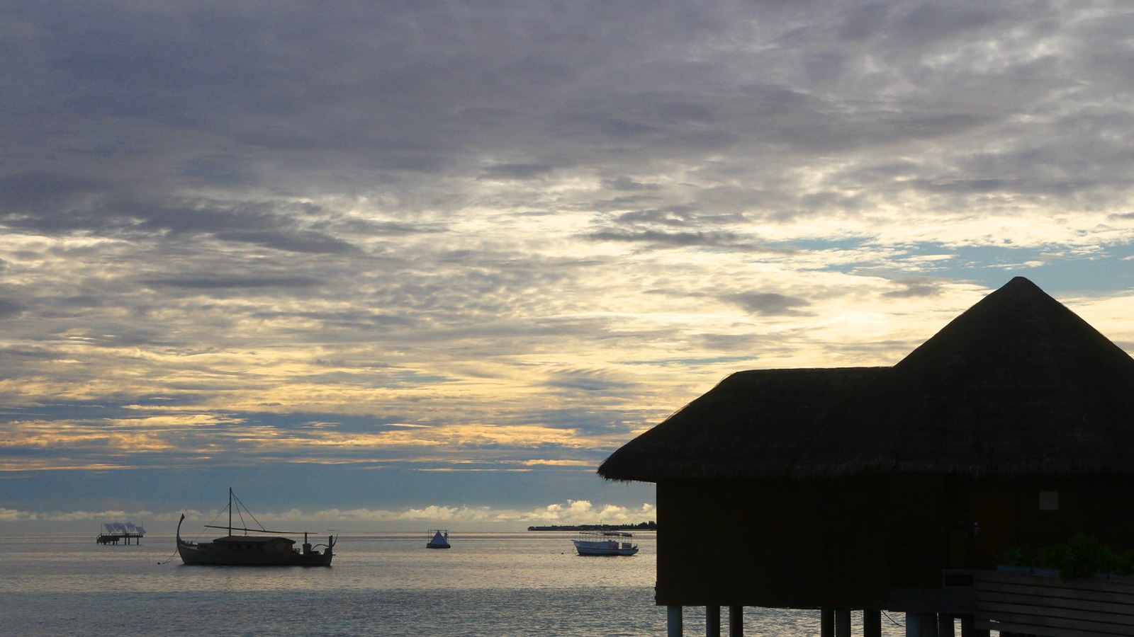 Overwater villa and traditional boat at a Maldives resort at sunrise