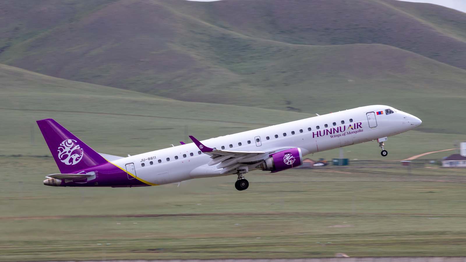 Hunnu Air Embraer 190 taking off from Ulaanbaatar with grassy hills behind