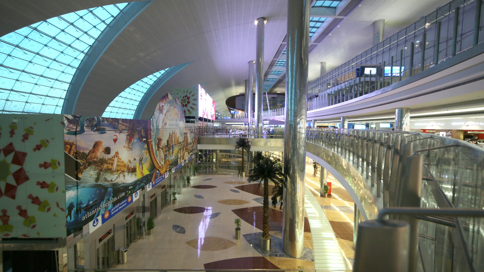 Interior of Dubai International Airport Terminal 3, showing the curved glass roof, passenger hall, and upper walkways