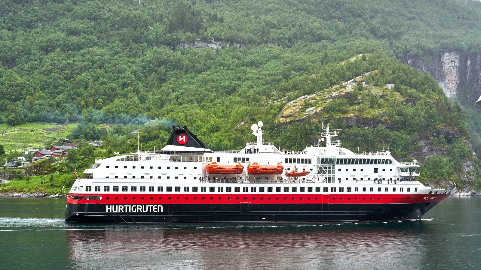 Hurtigruten ship Polarlys departing Geiranger with titles readable against a fjord shoreline