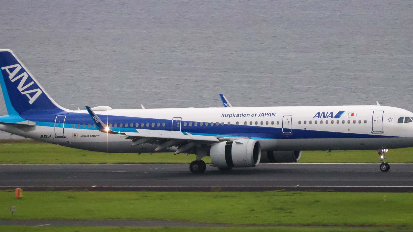 ANA Airbus A321neo in white and blue livery on the runway at Tokyo Haneda with Tokyo Bay behind.