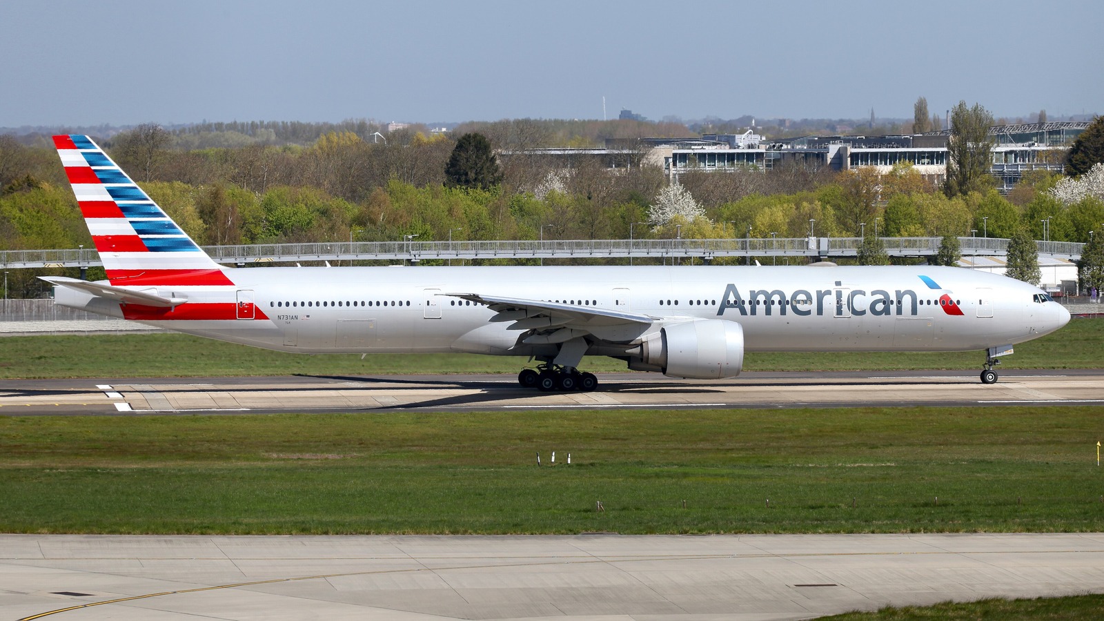 An American Airlines Boeing 777-300ER on a runway with the American titles and the flag tail clearly visible along the fuselage.