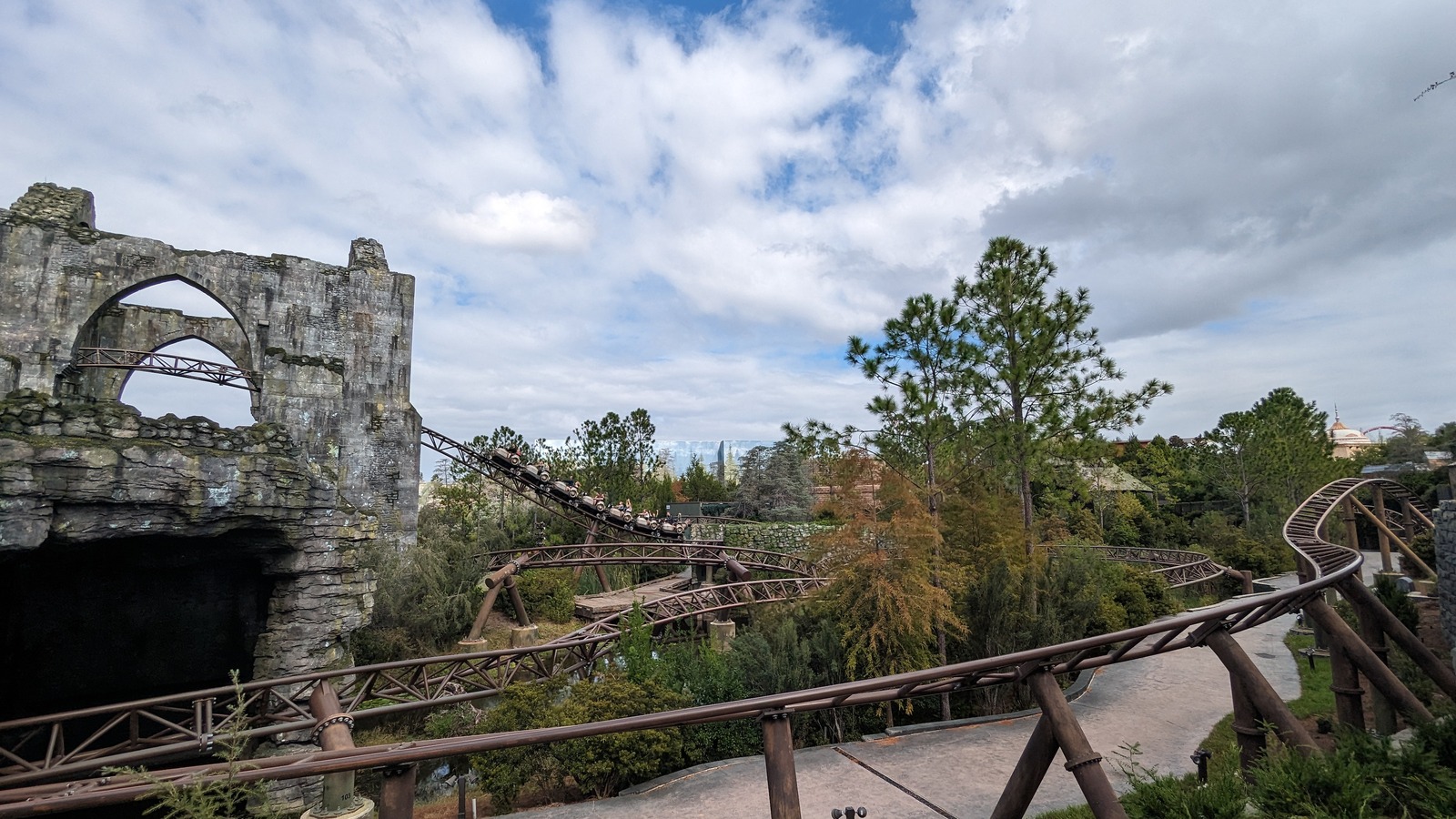Hagrid's Magical Creatures Motorbike Adventure coaster train on an outdoor track curve beside stone ruins in daylight