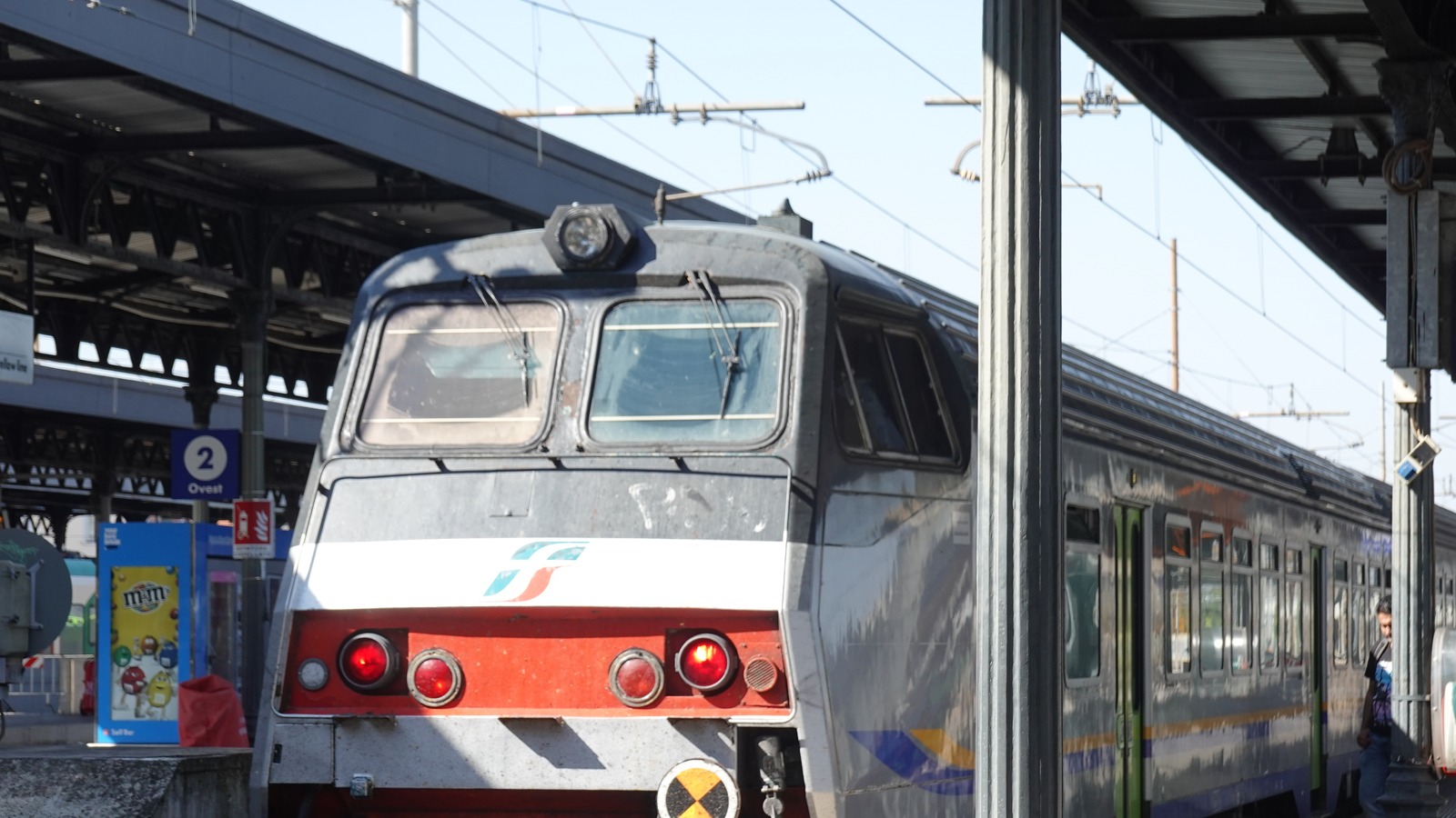 A Trenitalia train in Ferrovie dello Stato livery stands at a covered platform at Bologna Centrale station under overhead wires