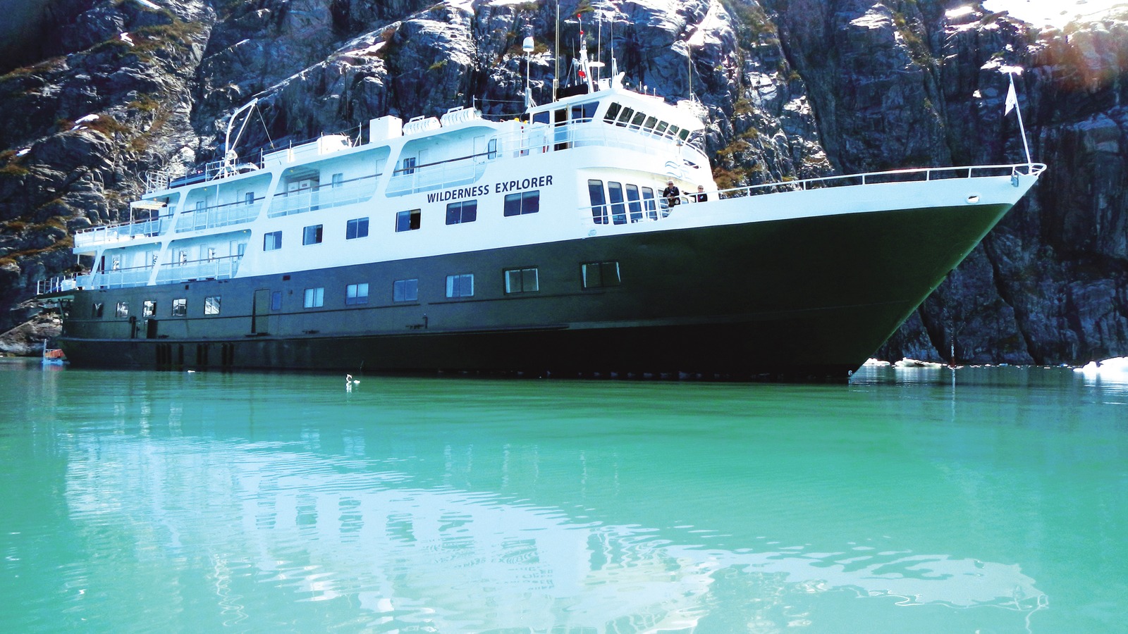 UnCruise Adventures expedition ship Wilderness Explorer in turquoise Alaska water, with WILDERNESS EXPLORER lettered on the white superstructure, photographed in the Glacier Bay area.
