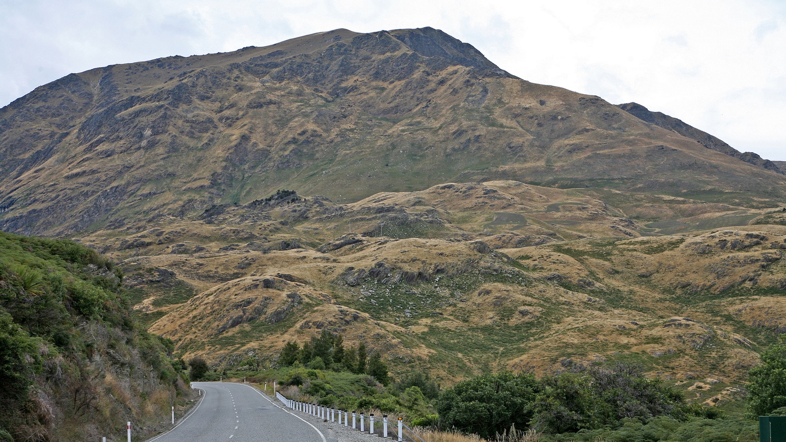 State Highway 6 winding through Haast Pass in New Zealand with tussock hills above the two-lane road