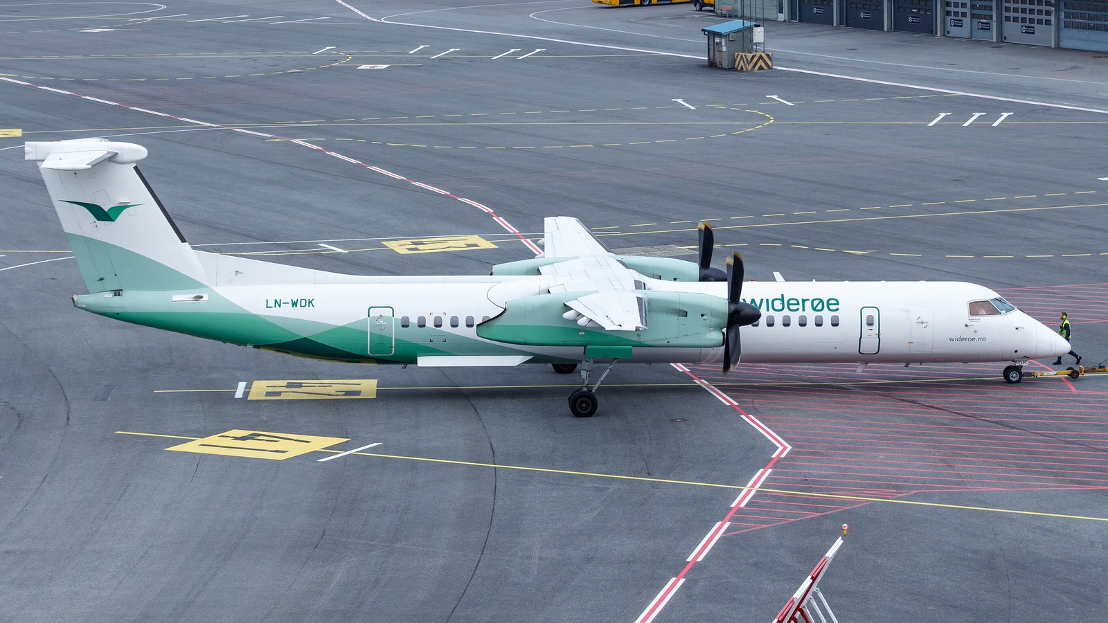 A white and green Widerøe Dash 8 Q400 turboprop, registration LN-WDK, being pushed back on an airport apron in daylight.