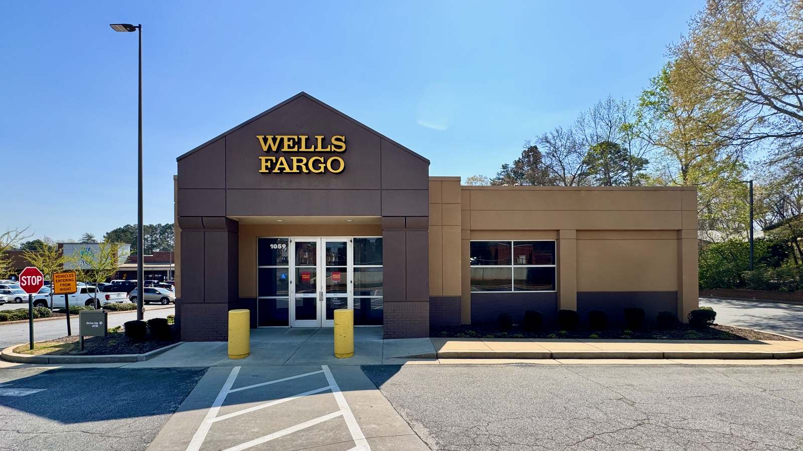 The front of a Wells Fargo bank branch with the Wells Fargo name in gold letters over glass entry doors on a clear day.