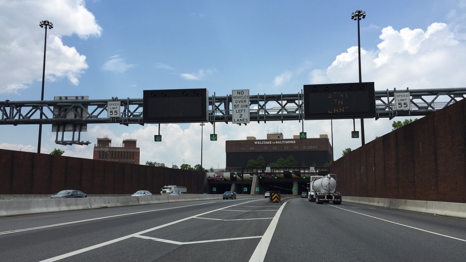 The southbound approach to the Fort McHenry Tunnel on Interstate 95 in Baltimore, with overhead lane use signals on a gantry, a Welcome to Baltimore sign above the portals and traffic descending toward the tunnel entrances