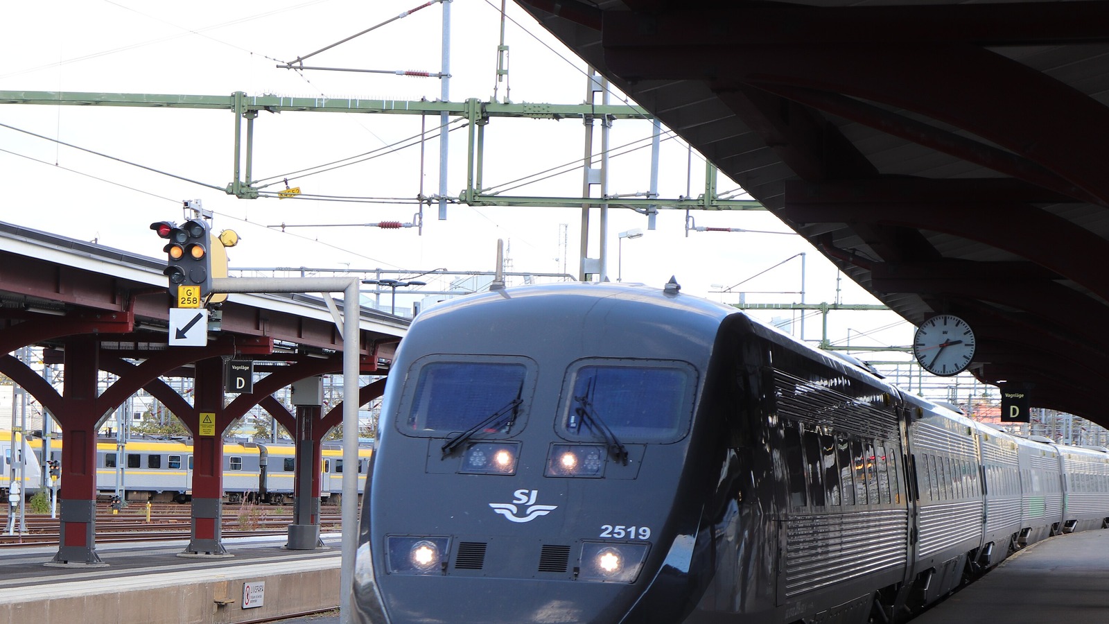 An SJ X2000 high-speed train with headlights on at a platform at Gothenburg Central Station under a red steel canopy.