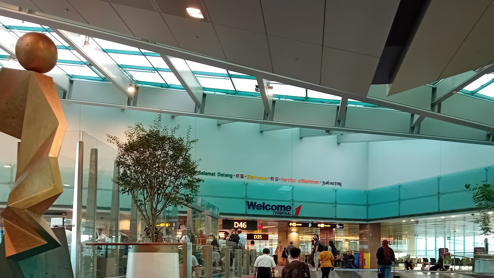 Arrivals hall at Sydney Airport Terminal 1, with the Welcome Terminal 1 sign, gates D46 and D35, and travelers with luggage.