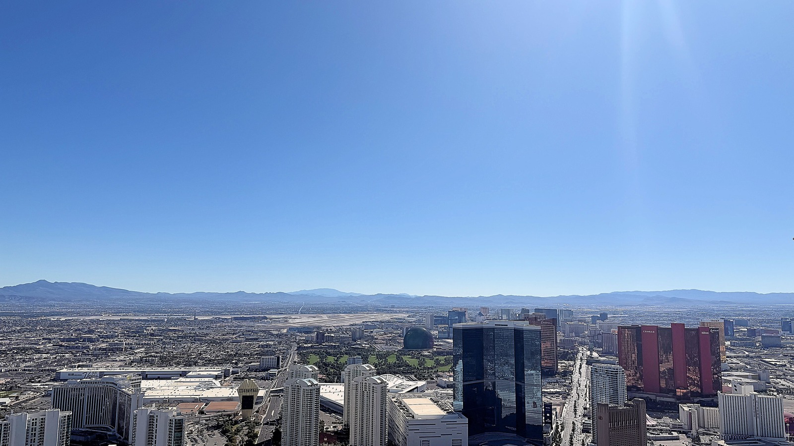 The Las Vegas Strip and valley seen from The STRAT observation deck on a clear day, with resort towers along Las Vegas Boulevard and mountains on the horizon.