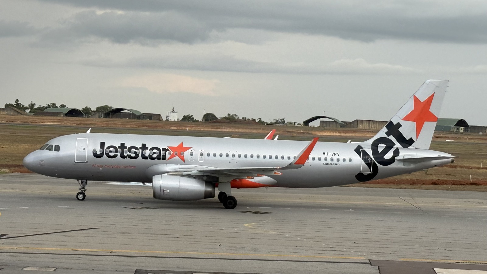 A Jetstar Airways Airbus A320, registration VH-VFV, taxiing under an overcast sky with the Jetstar titles, orange star tail and Airbus A320 fuselage marking visible.