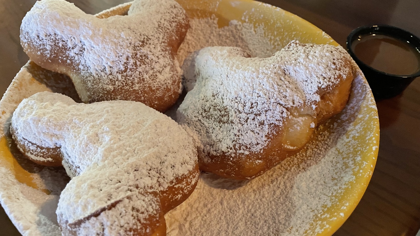 Three powdered-sugar Mickey-shaped beignets on a yellow plate at Disney's Port Orleans Resort French Quarter