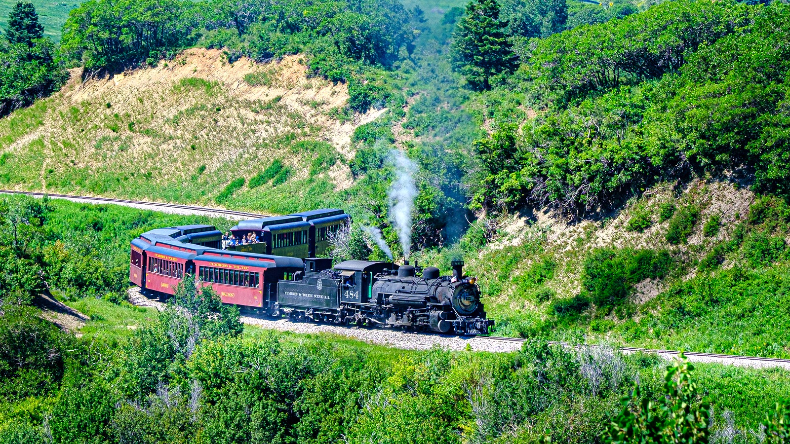 Cumbres and Toltec locomotive 484 pulling red passenger cars through green mountain scenery in July 2024