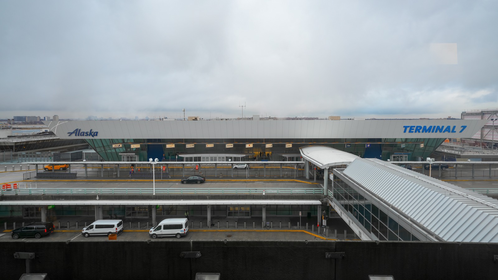 Daytime exterior of JFK Airport Terminal 7 with labeled Terminal 7 fascia, curbside lanes, and lower garage levels