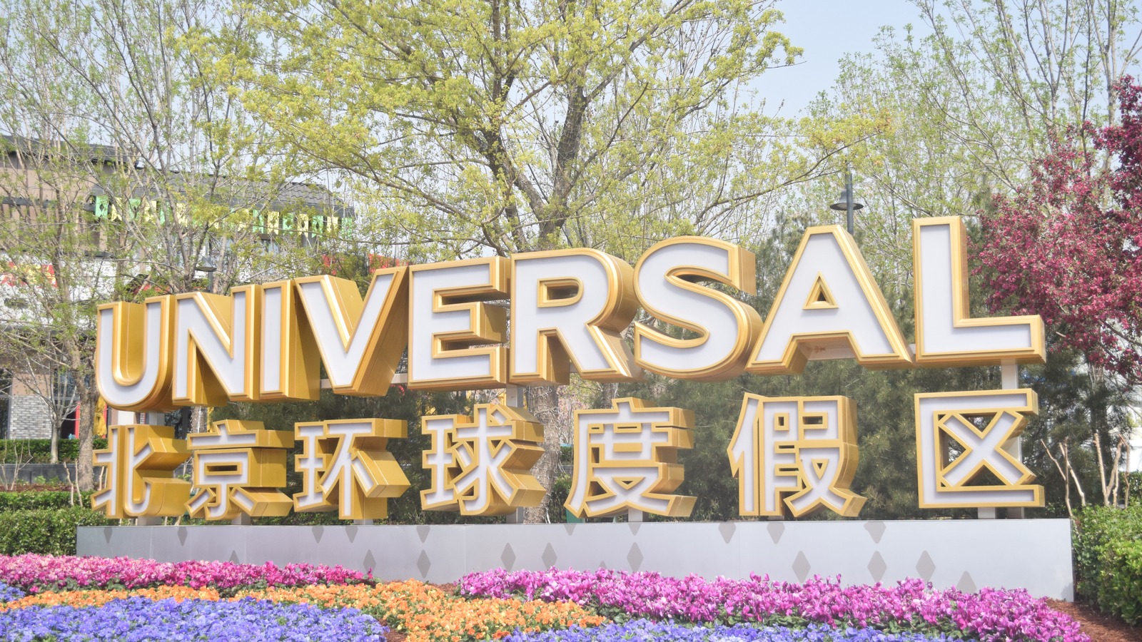 Universal Beijing Resort entrance sign with English and Chinese lettering above flower beds in daylight