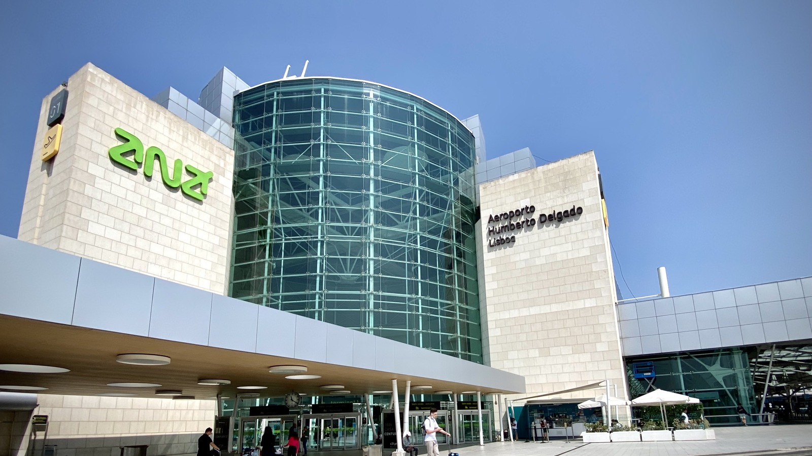 Exterior of Humberto Delgado Airport in Lisbon with ANA signage and the arrivals curb where taxis pick up passengers.