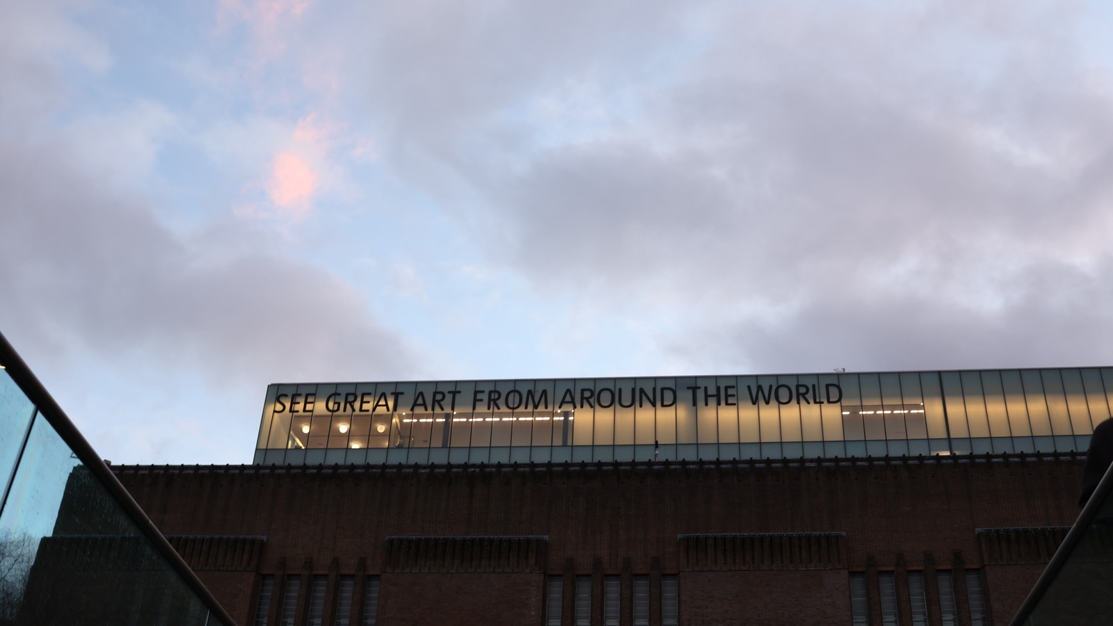 Exterior of Tate Modern in London with the glass gallery reading See Great Art From Around the World