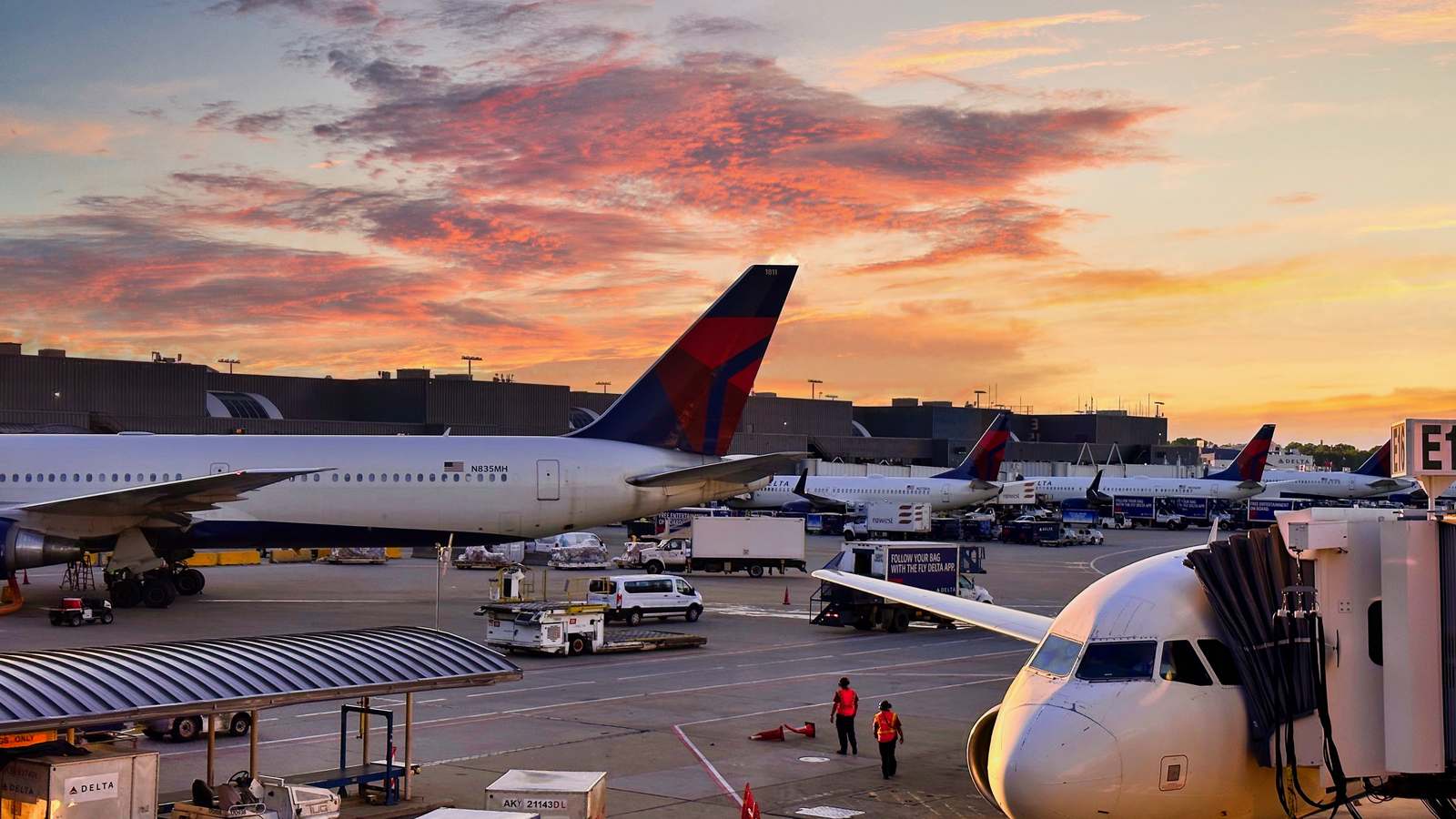 Delta jets parked at gates at Hartsfield-Jackson Atlanta International Airport under an orange sunset sky, with ground vehicles on the apron.