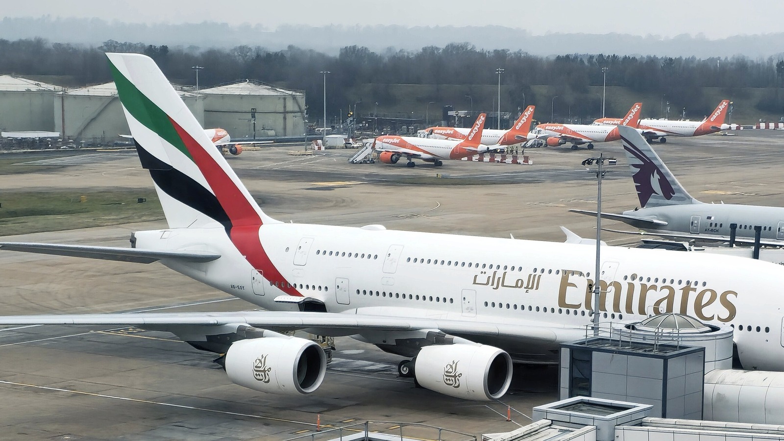An Emirates Airbus A380 on a stand at London Gatwick with the Emirates titles along the upper deck and easyJet aircraft parked behind it.