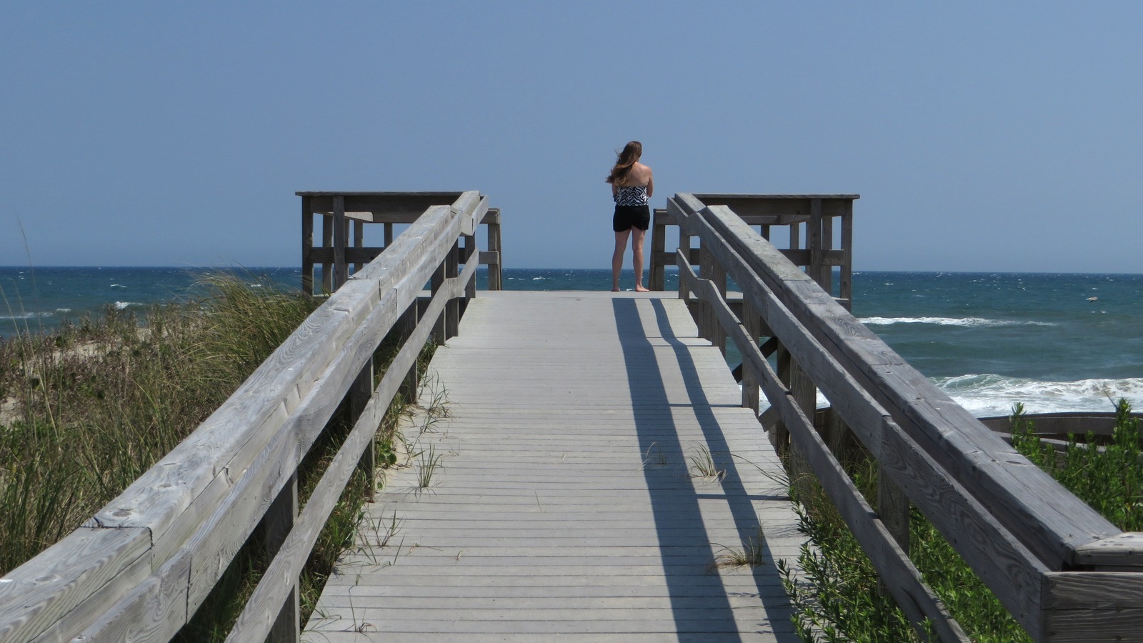 Wooden boardwalk leading to the Atlantic Ocean at Cape Hatteras National Seashore, with dunes and a visitor at the beach overlook