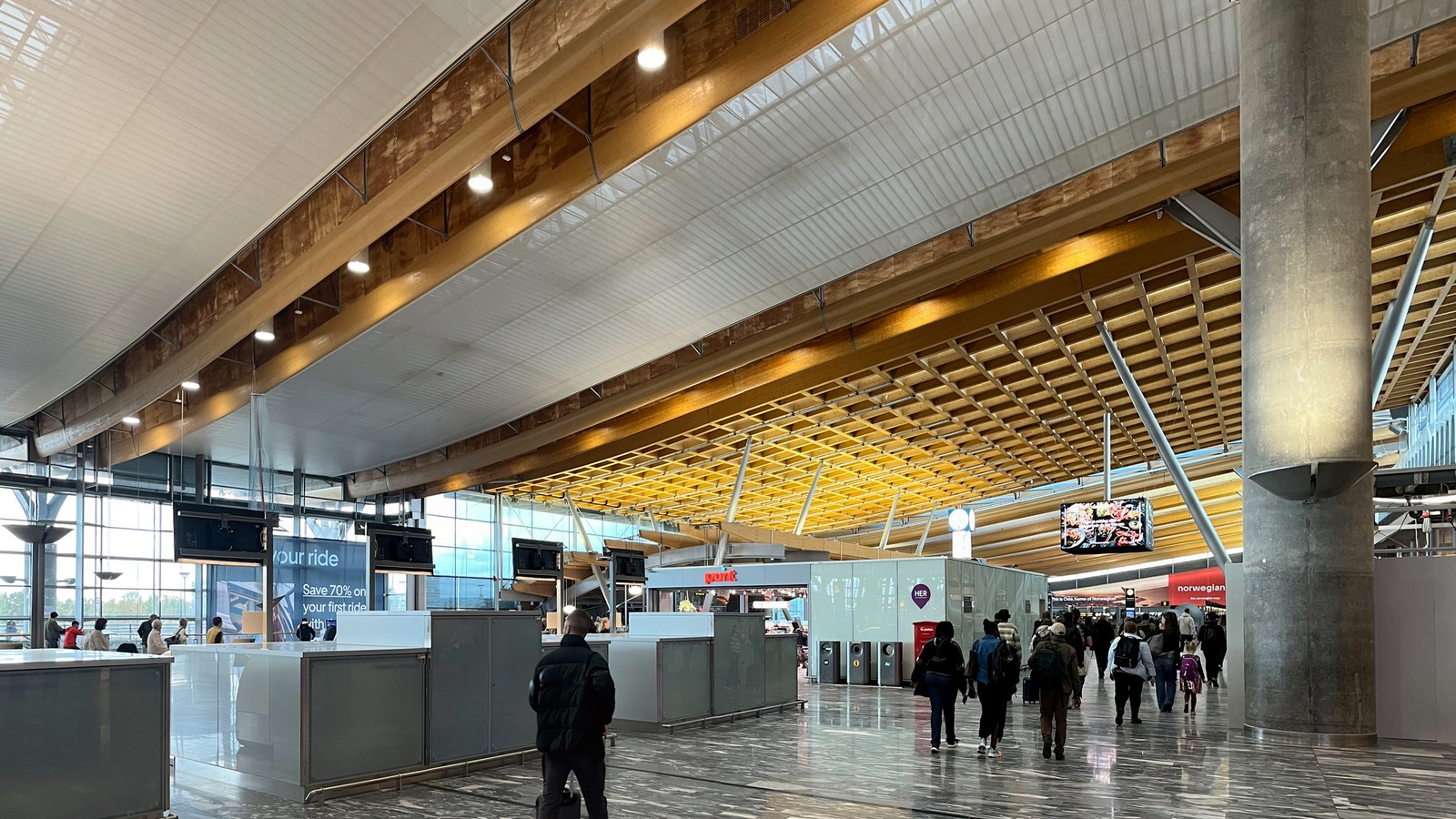 Passengers walking through the wooden roofed terminal at Oslo Airport Gardermoen