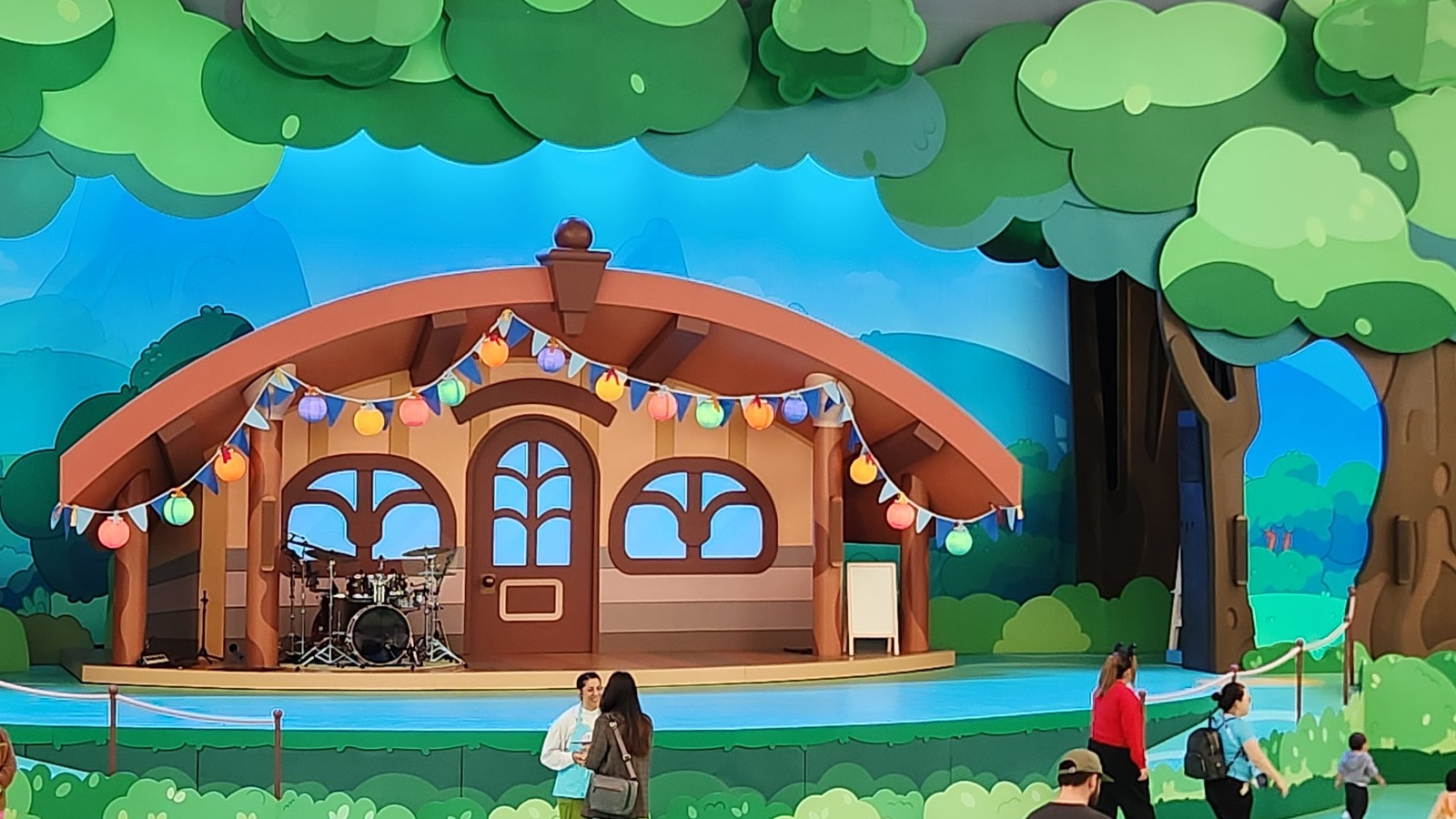 The Bluey's Best Day Ever stage set in the Fantasyland Theatre at Disneyland, a cartoon house with bunting and paper lanterns against a painted outdoor backdrop