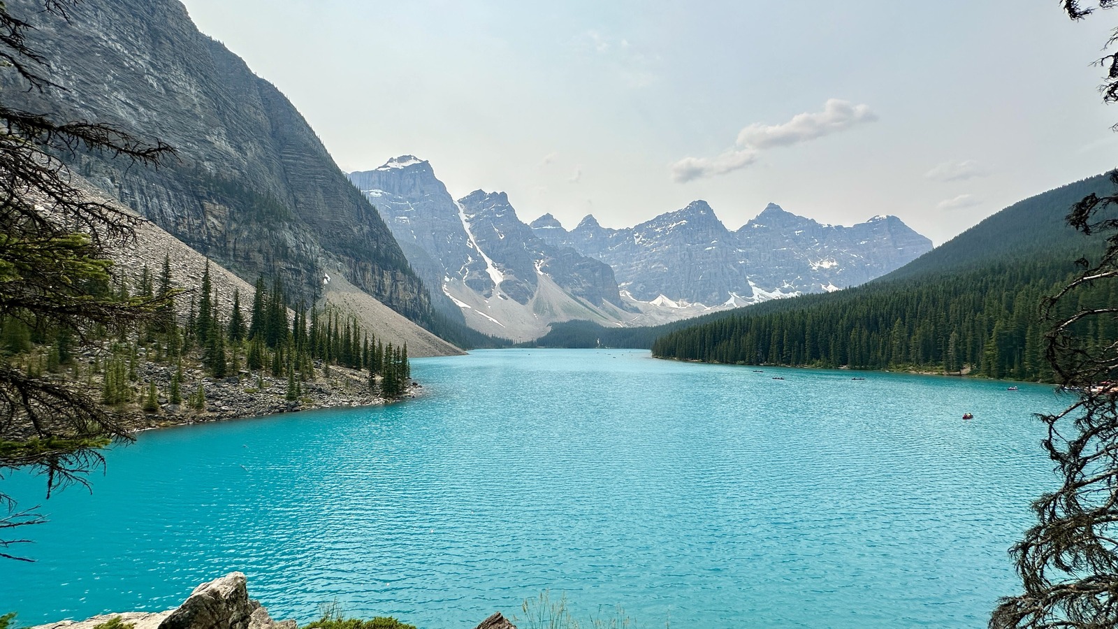 Moraine Lake in Banff National Park seen along its length, turquoise water framed by larch and spruce with the grey summits of the Valley of the Ten Peaks rising at the far end and small boats on the water.