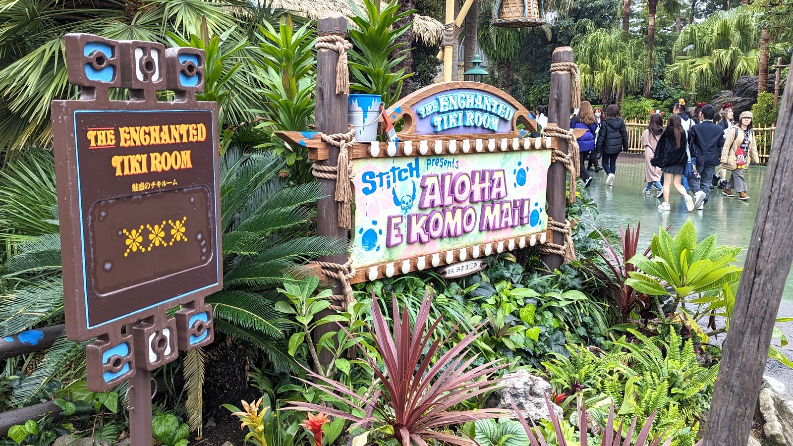 Tokyo Disneyland Enchanted Tiki Room signs for Stitch Presents Aloha E Komo Mai beside the Adventureland queue