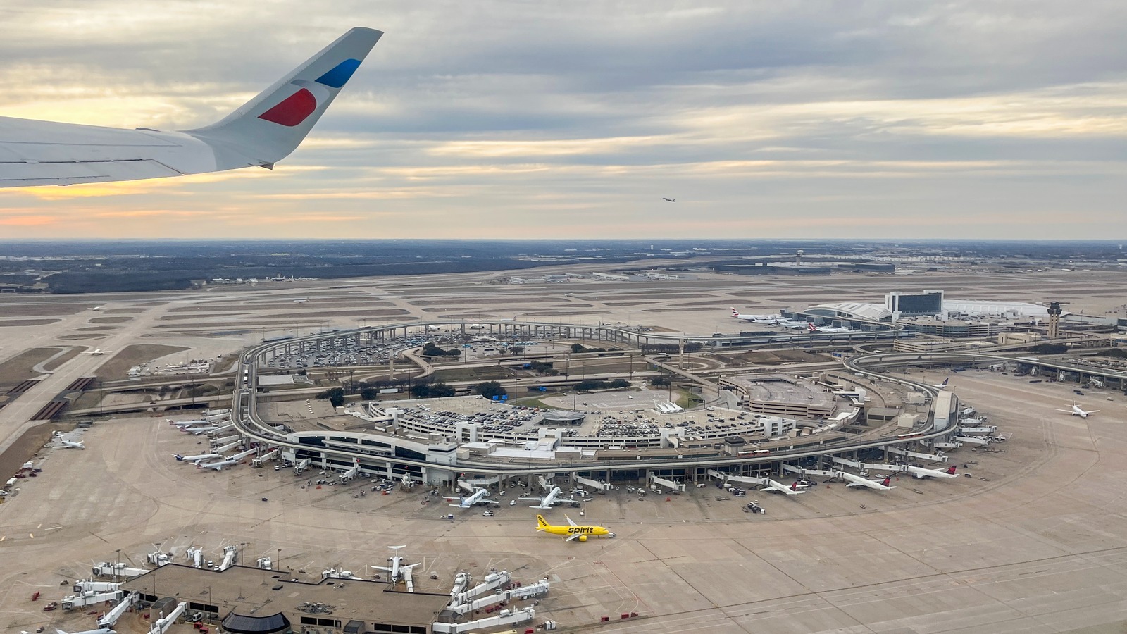 Aerial view of Dallas Fort Worth International Airport Terminal E, parking garage, and curbside roadways during takeoff