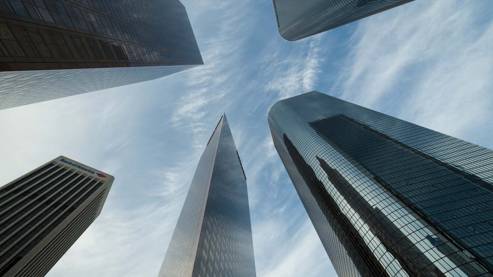 Glass office towers in Downtown Los Angeles seen from street level against a blue sky with thin clouds.