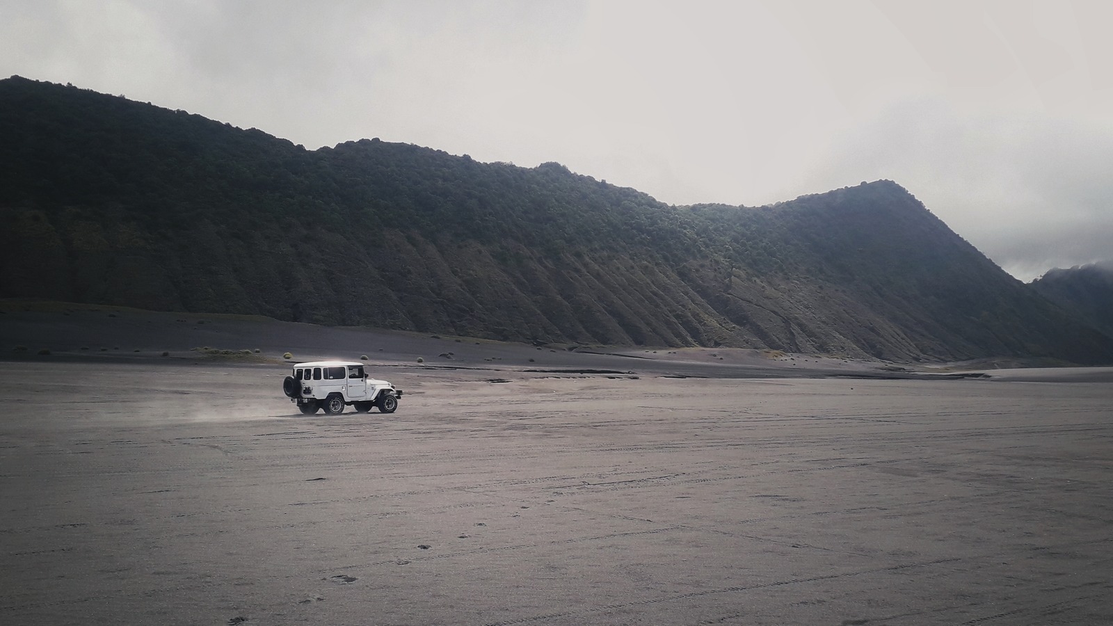 White jeep crossing the Sea of Sand below the caldera wall at Mount Bromo in East Java, Indonesia