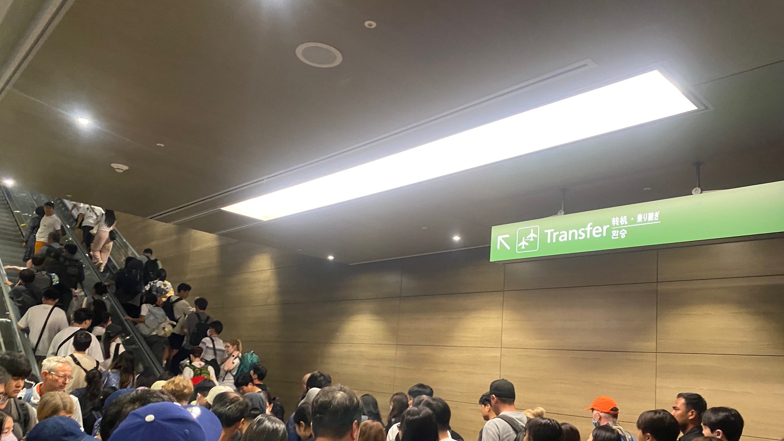 Crowds on an escalator under a Transfer sign at Incheon International Airport