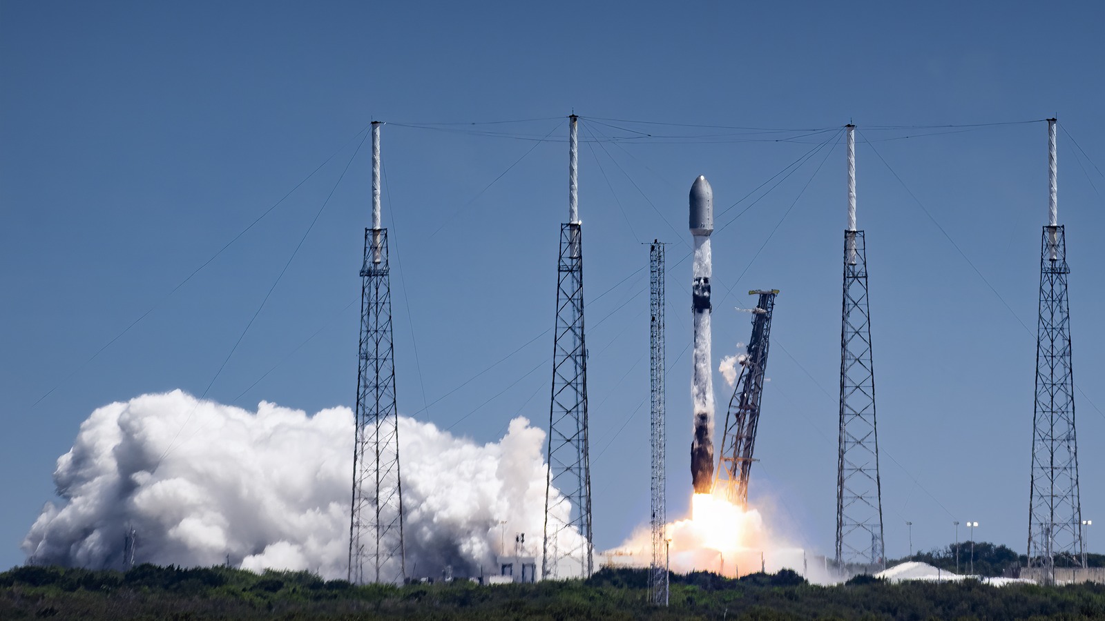 A Falcon 9 rocket lifting off in daylight from Space Launch Complex 40 at Cape Canaveral, with launch towers and a white exhaust cloud.