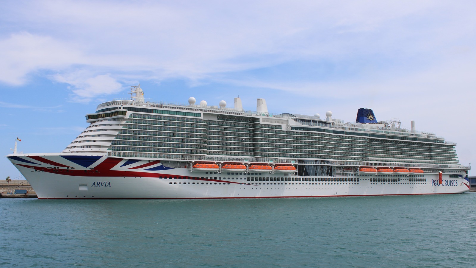 P&O Cruises ship Arvia docked in Barcelona, Spain, on July 3, 2023, showing the Union Jack bow livery, the ARVIA hull name, and P&O Cruises on the stern.