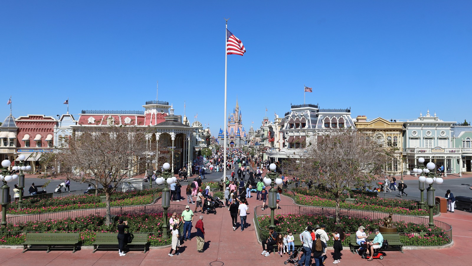 An elevated daytime view down Main Street USA at Magic Kingdom in Walt Disney World, with the flagpole in the foreground and Cinderella Castle at the far end under a clear blue sky
